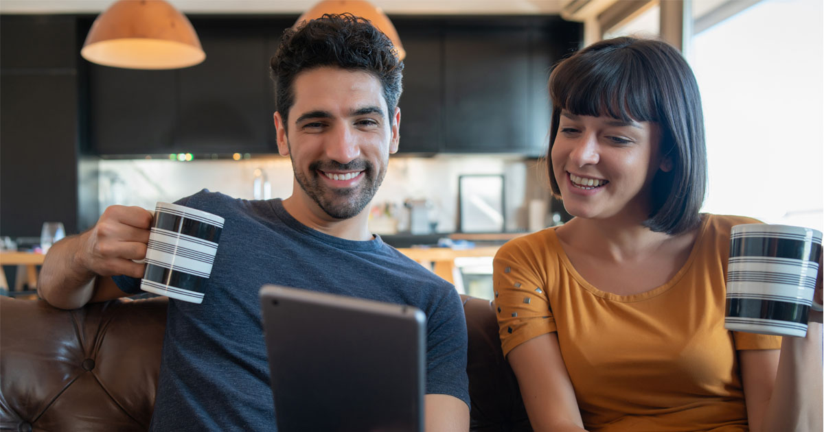Portrait of young couple on a video call with digital tablet while sitting on couch at home. Stay at home. New normal lifestyle concept.