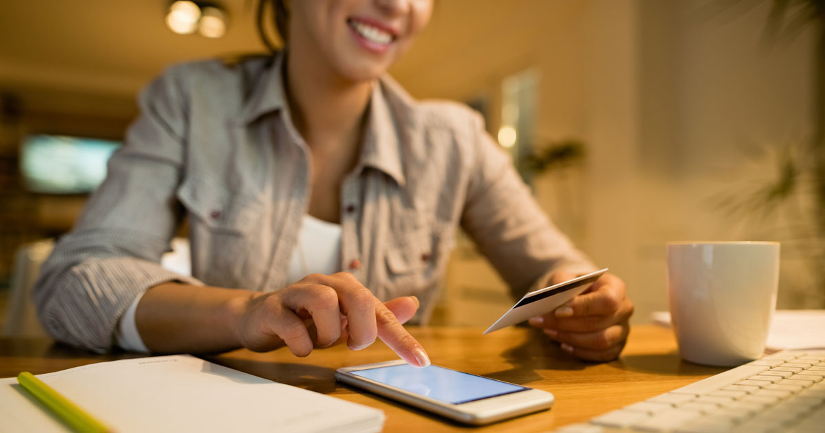 Close-up of woman sing credit card and smart phone while shopping online at night at home.